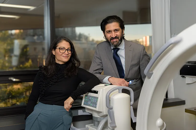 Two professionals in office attire stand by medical equipment, smiling confidently in a well-lit room.