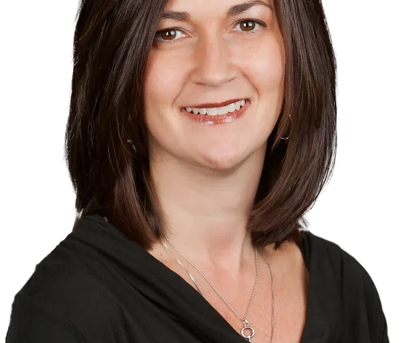 Smiling woman in a black top with layered necklace, shoulder-length brown hair, facing forward.